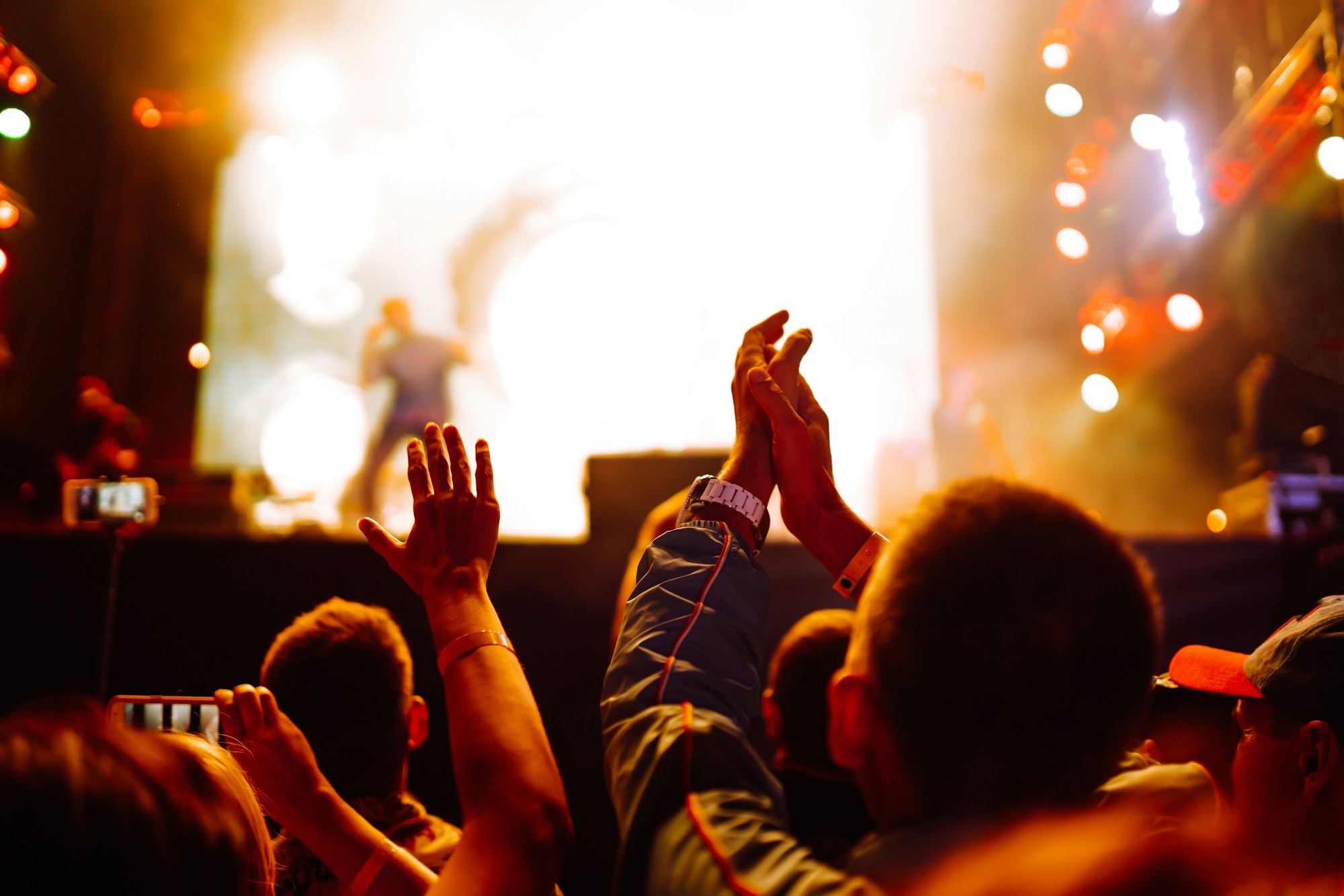 Сrowd with raised hands at music festival. Fans enjoying rock concert with light show clapping hands